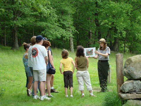 A ranger holding up an image with a group of visitors looking on.
