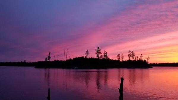 A sunset fades over a lake from deep purple to pink. A silhouette of an island is in the background.