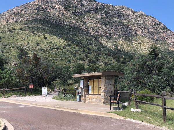 A stone kiosk with trail information marks the beginning of a trail in a desert mountain landscape.