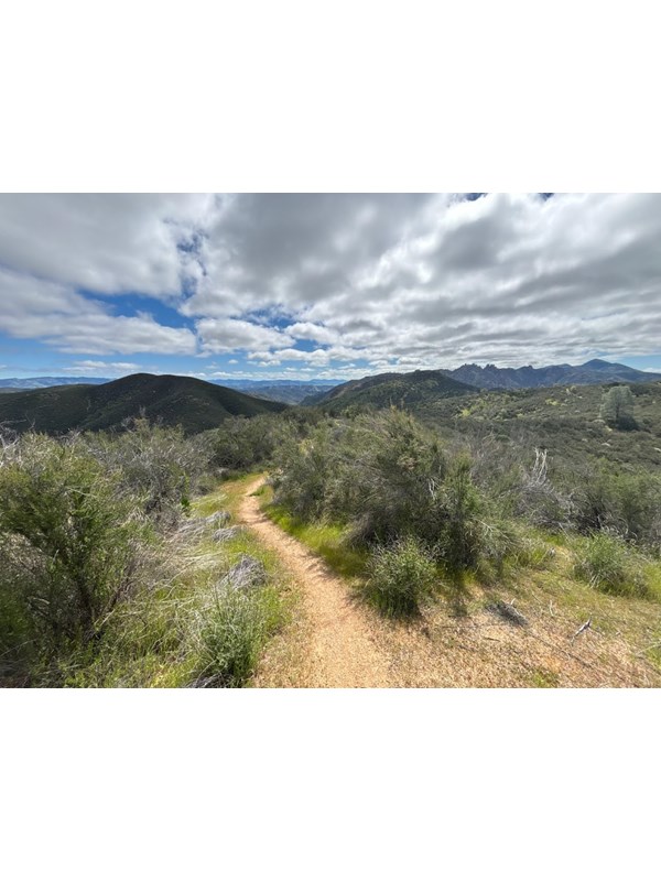 Trail leading through chaparral covered hills overlooking rock formations in the distance.
