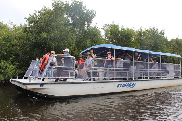 Large open-air white boat with a blue canopy carrying passengers through murky water