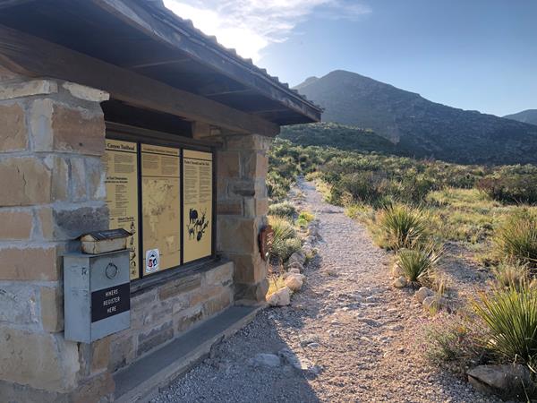 A stone kiosk with trail information in a desert mountain landscape