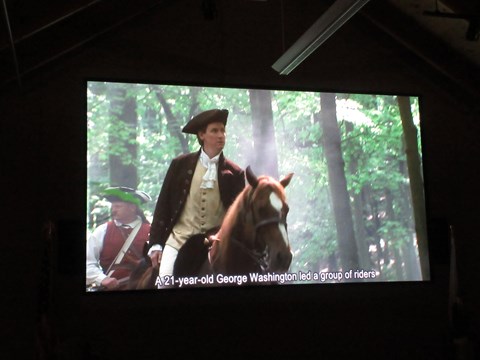 Screen shot of a movie showing a young colonial officer on a horse followed by a man in ar red vest