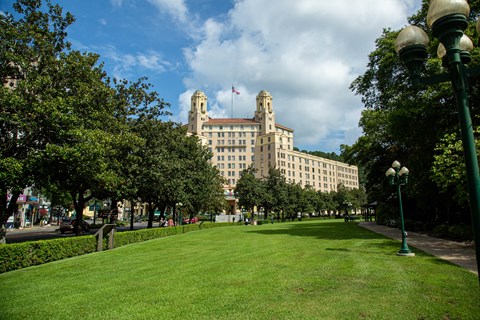 A lush, green lawn lays before a tall, wide, tan hotel building.