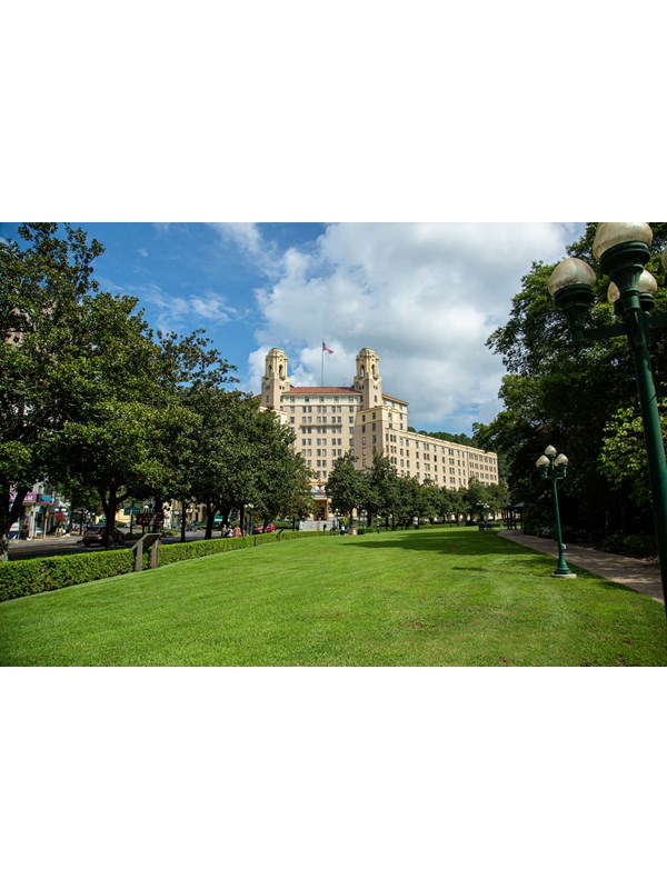 A lush, green lawn lays before a tall, wide, tan hotel building.