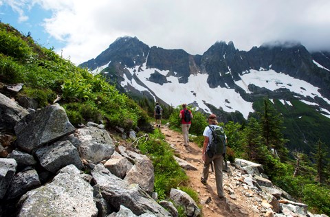 Two hikers walk along a trail with mountains in the distance.