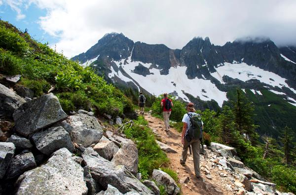 Two hikers walk along a trail with mountains in the distance.