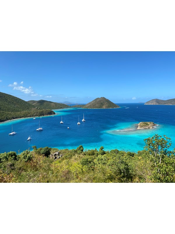 Distant boats dot turquoise water of varying shades on a brilliantly sunny day.