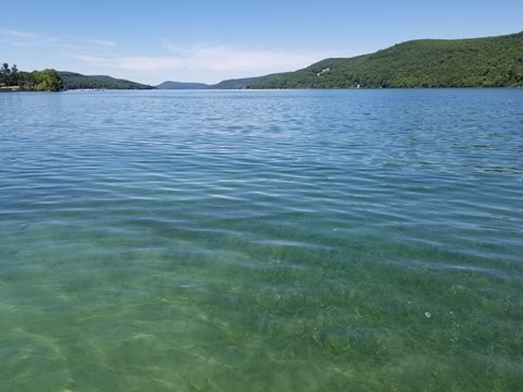 A lake with clear, blue-green water and distant tree-covered hills.