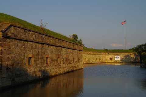The setting sun lights a stone fort wall where a US flag flies on a high staff.