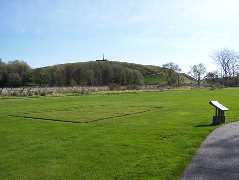 trail passing an informational sign with a monument on a hill in the background