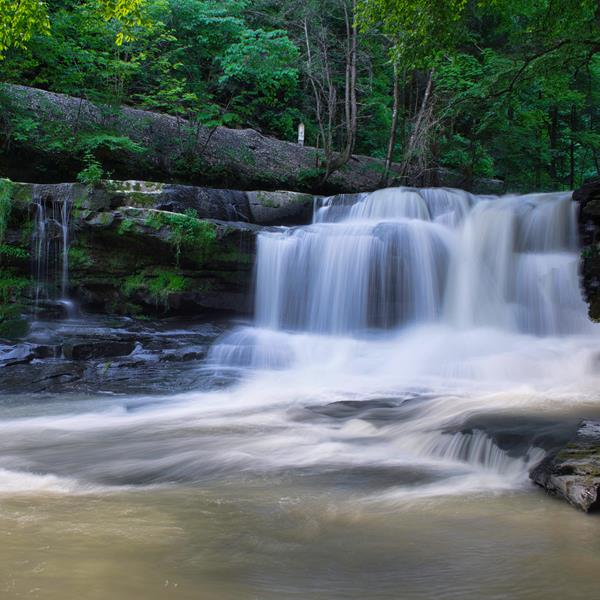 A wide cascade of water flowing down a rocky drop-off into a rock filled pool
