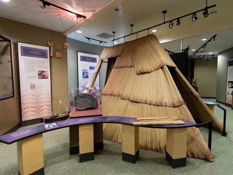 A color photo of an inside room with a windy table. There’s a structure made from organic mats.