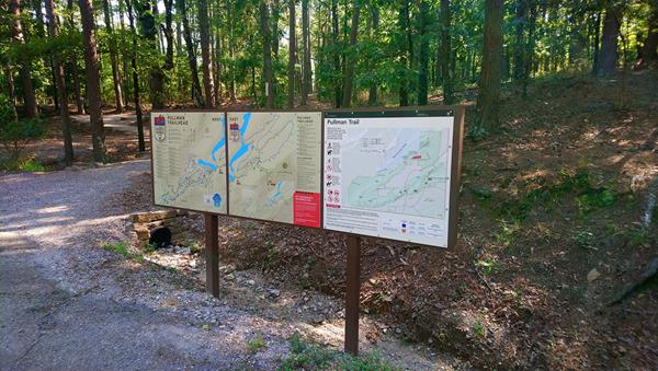 Three trail head signs line the front of a trailhead that leads into the forest.