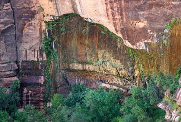 A large, arch shaped alcove streaked with dark shades of orange on red rock.