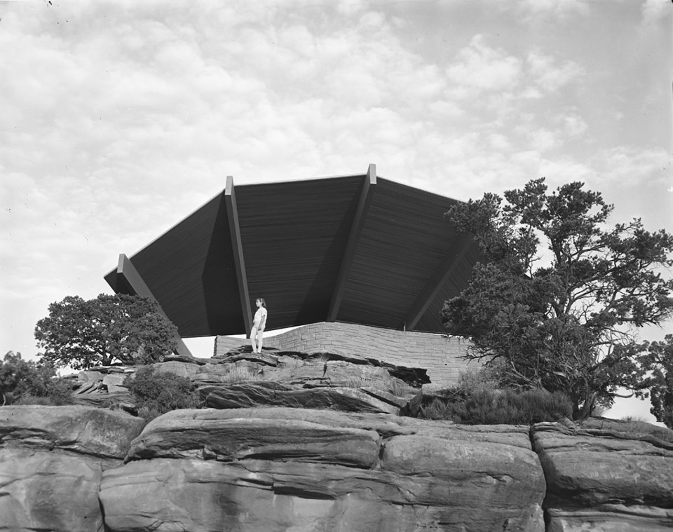 Sandstone brick shelter with cantilevered wooden roof fanning out above it.