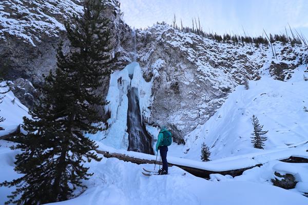 A skier looks up at the ice formations surrounding a frozen waterfall.