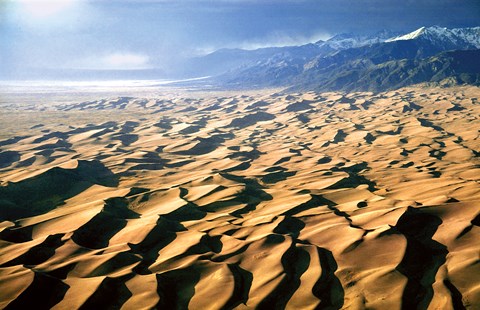 Aerial view of the 30-square-mile dunefield at sunset with a snow-capped mountain in the distance