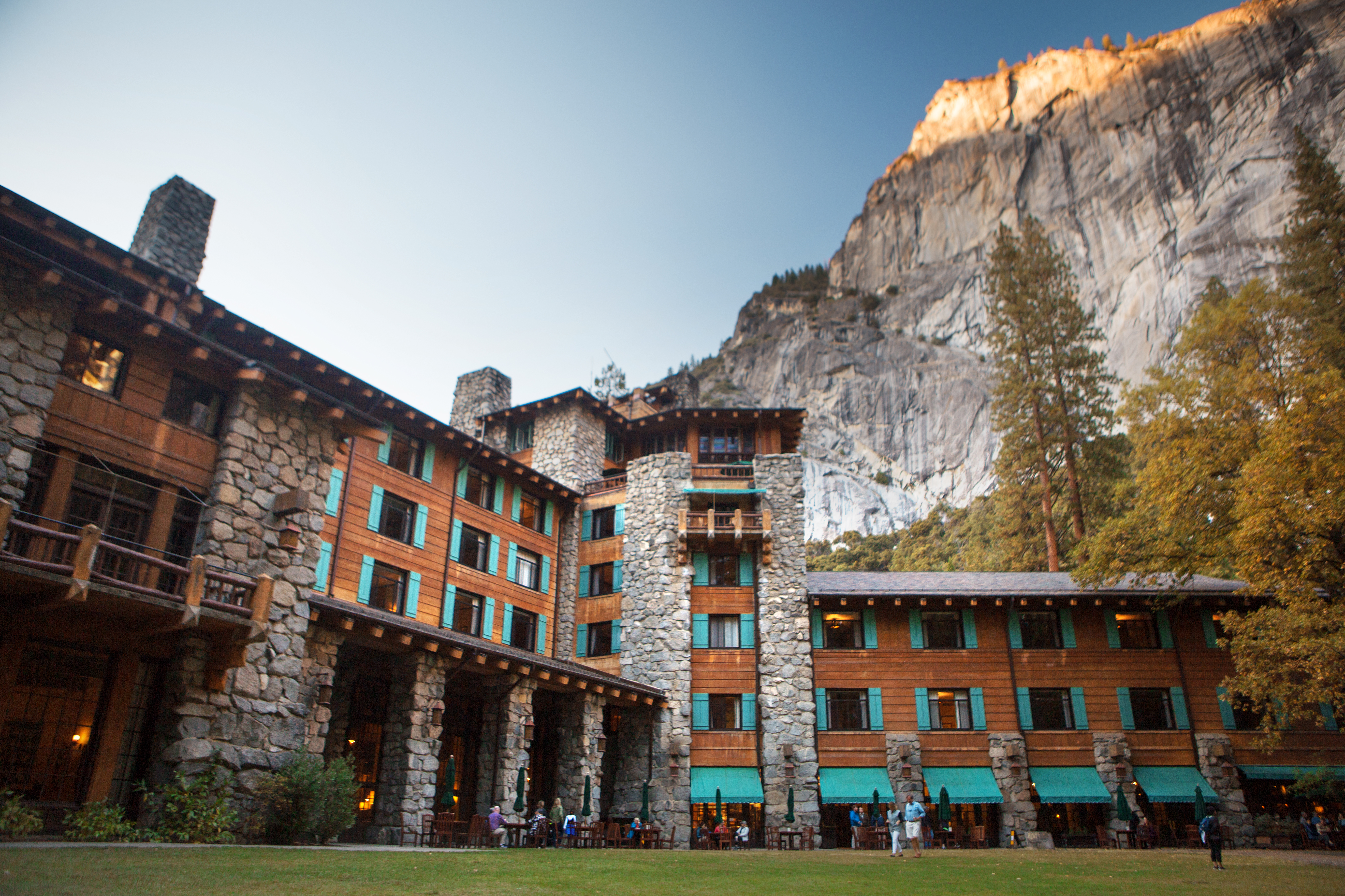 A sheer cliff face serves as a backdrop behind a building made of stone and wooden planks.