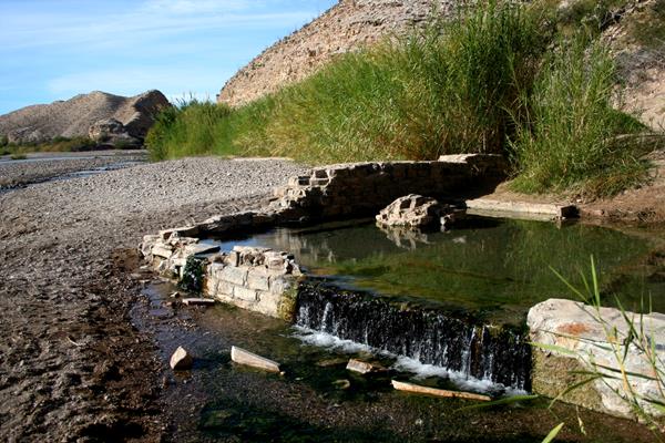 A pool of fresh water pours out of the ruined foundation of a desert hot spring bath house.