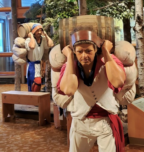 Mannequins dressed in historic clothing carrying heavy looking bales of trade goods.