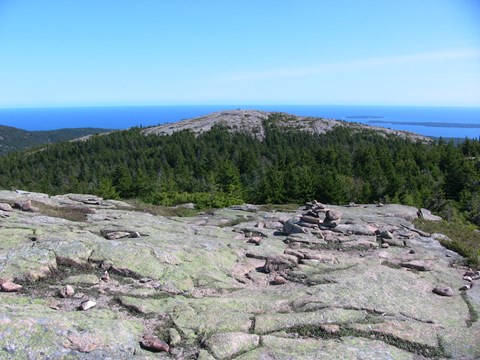 a view from a rocky summit looking out to another rocky summit, ocean, and blue sky