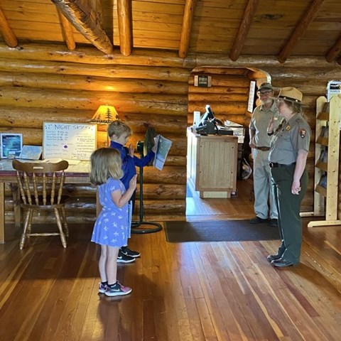 A ranger stands in front of two children and all have their right arms raised.