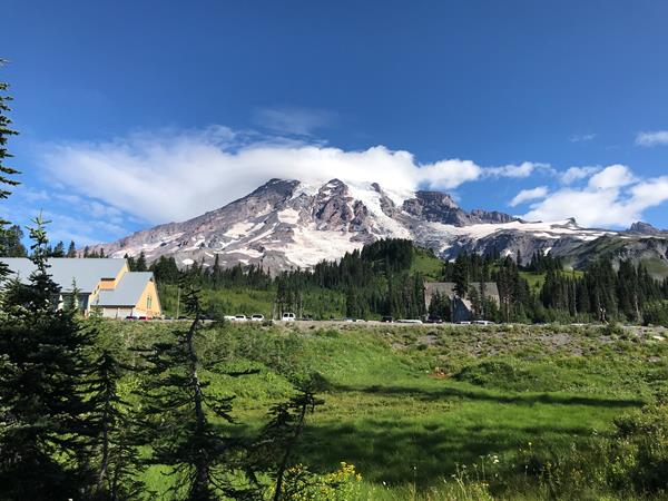 Buildings and a road tucked against a mountain slope surrounded by green meadows.