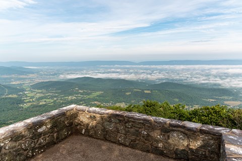 A stone platform with a view of a valley below and blue mountains beyond.