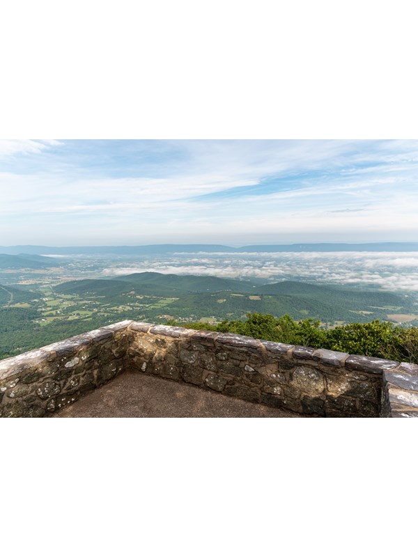 A stone platform with a view of a valley below and blue mountains beyond.