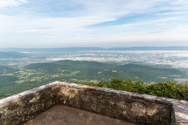 A stone platform with a view of a valley below and blue mountains beyond.