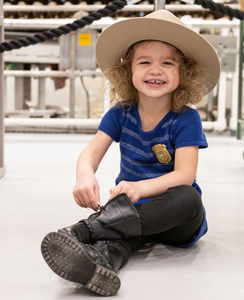 A young girl smiling for the camera, wearing a ranger hat and Junior Ranger badge.