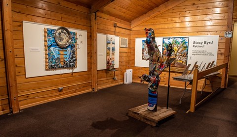 An interior view of a room with a large sculpture on the floor and colored art on the walls.