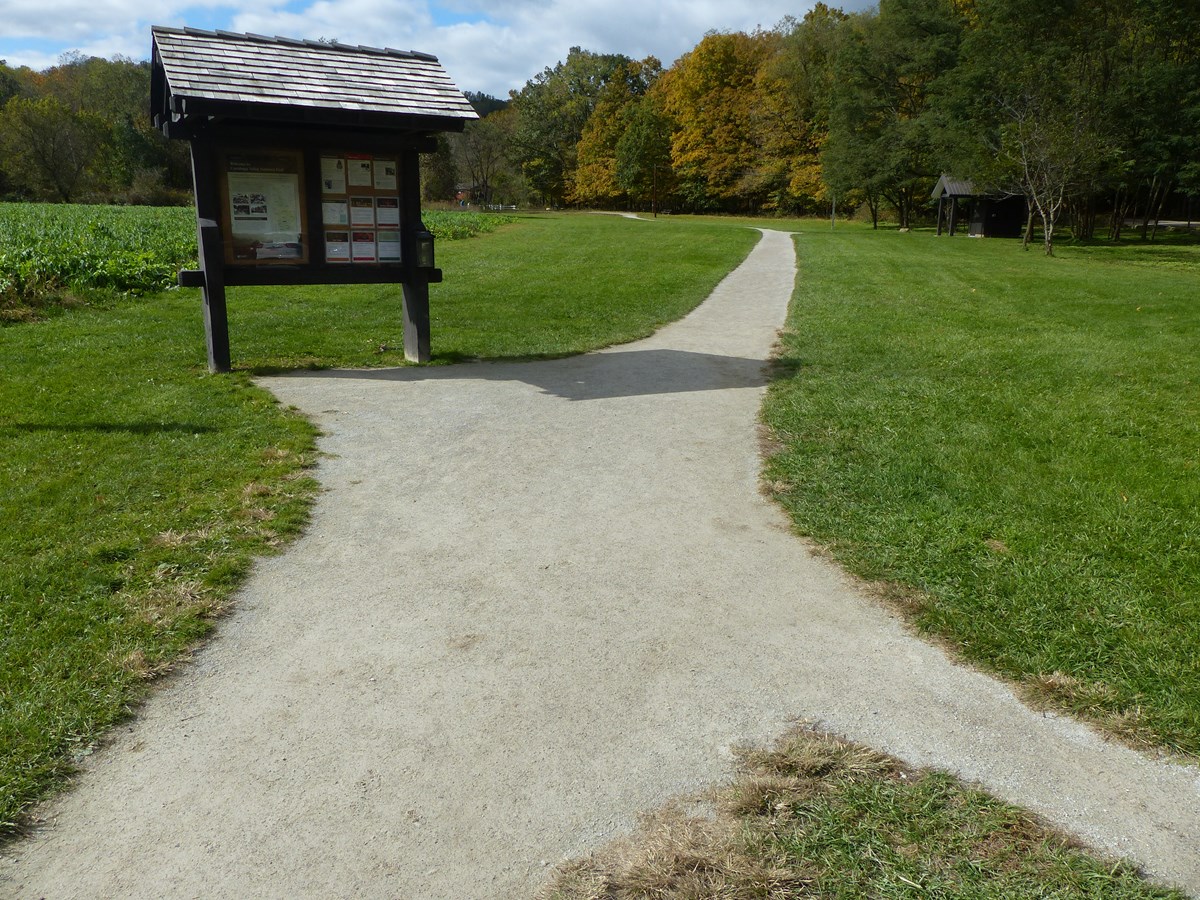 Firm, flat, unpaved trail curves from a kiosk, past restrooms, to the distant red bridge in the trees.