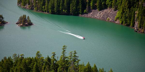 A motorboat on a green lake surrounded by mountains.