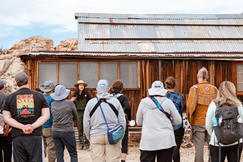 A park ranger talks to a group of visitors in front of a rustic building