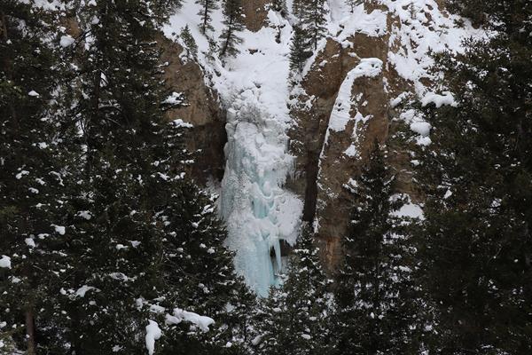 Icicle formations encase a waterfall surrounded by columns of rock.