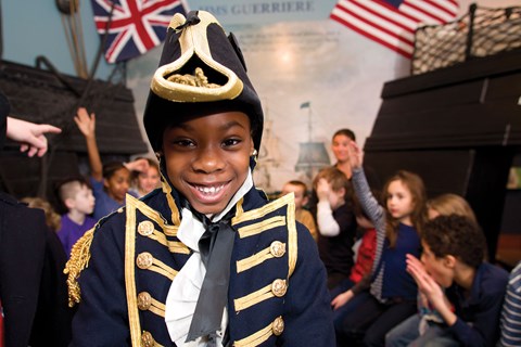 Young girl in a blue 1812 captain's uniform while kids learn in background
