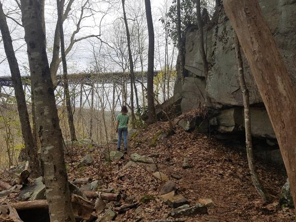 A hiker on rocky trail about to pass under a large bridge