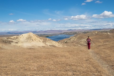 A lone hiker standing on an arid plateau with water and mountains in the distance.