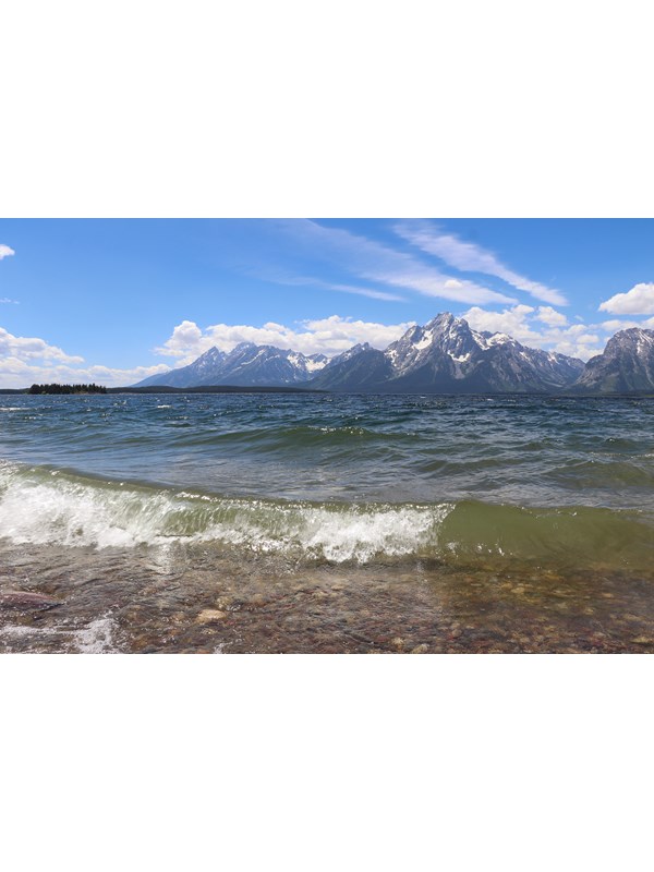 Waves crash on the shore of a lake at the base of a mountain range.