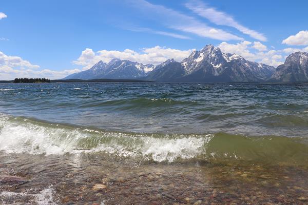 Waves crash on the shore of a lake at the base of a mountain range.