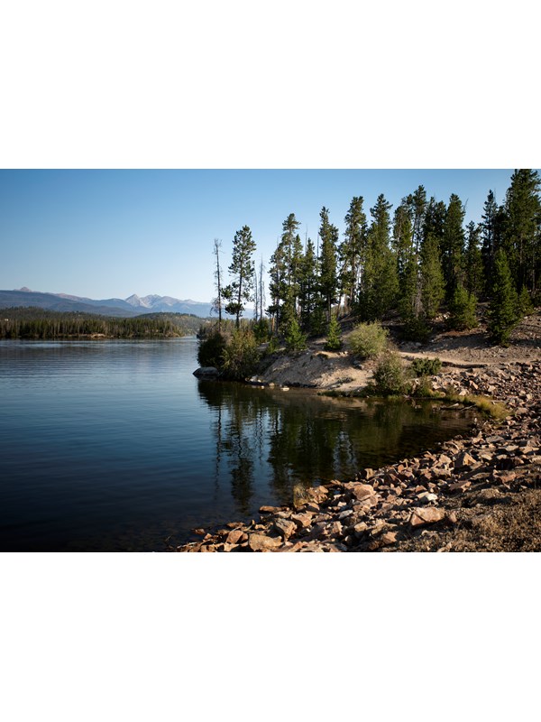 a rocky shore along a blue lake lined with trees