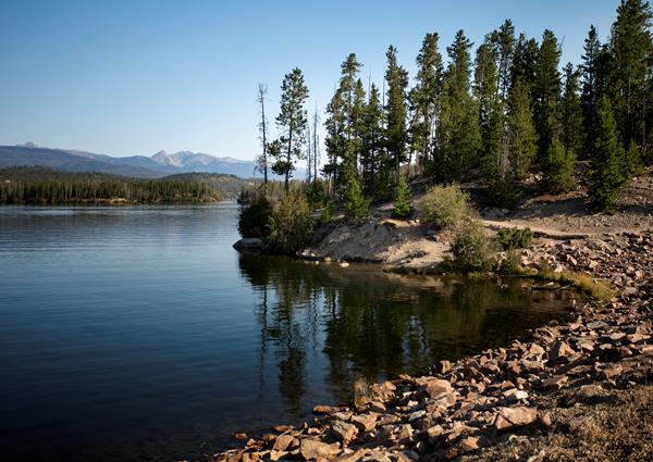 a rocky shore along a blue lake lined with trees