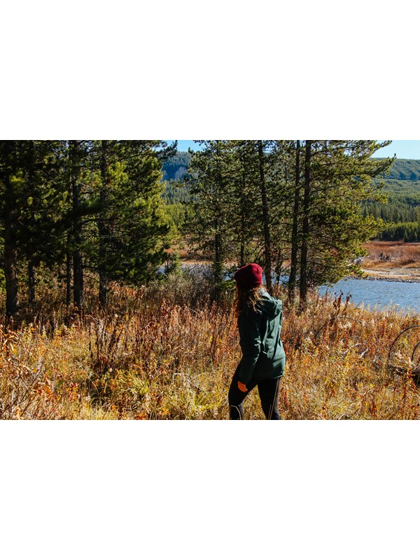 A female hiker walks along a wooded trail by a river.