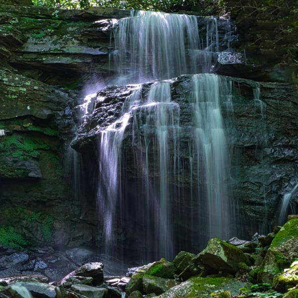 Water flowing gently over stepped sandstone rocks sticking out from a rocky face