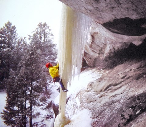 A person climbing an ice formation hanging from the granite.