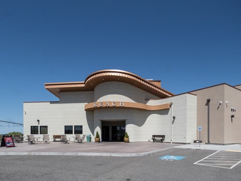 Color photograph of a cement brick building with an ornate copper roof. A sign reads "REACH."