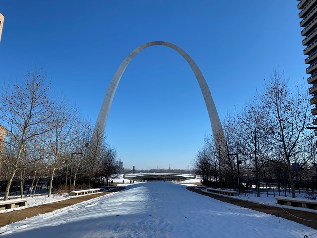 The stainless steel Gateway Arch rises 630 feet over snowy grounds against a clear blue sky