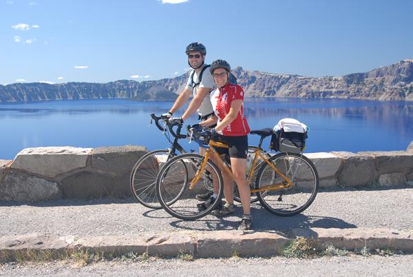Two visitors on bikes with Crater Lake in the background.